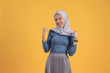 happy asian indonesian muslim woman cheerful expression with clenched fist on isolated yellow background