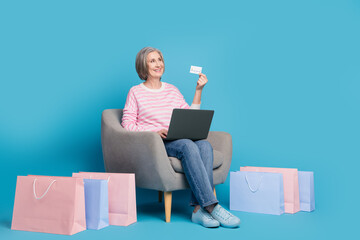 Wall Mural - Full body photo of nice senior woman sit armchair netbook shopper credit card wear trendy striped outfit isolated on blue color background