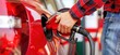 © Nanda - Close up of a man filling up his red car with fuel at a gas station.