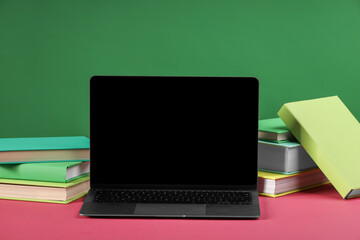 Wall Mural - Many colorful books and laptop on pink table against green background