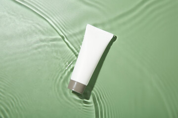 Wall Mural - Tube with cream in water on light green background, top view. Cosmetic product