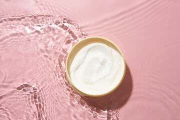 Wall Mural - Cosmetic product. Jar with cream in water on pink background, top view