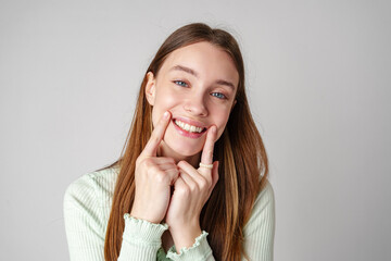 Wall Mural - Young Woman With Long Brown Hair Smiles and Touches Her Cheeks