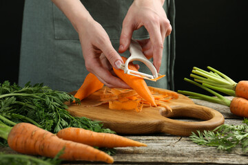 Wall Mural - Woman peeling fresh carrot at wooden table, closeup