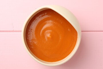 Delicious baby food in bowl on pink wooden table, top view