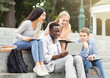 © Prostock-studio - Group of international cheerful students studying together, using laptop at park, sitting on stairs