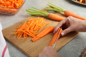 Wall Mural - Woman cutting fresh carrot at gray textured table, closeup