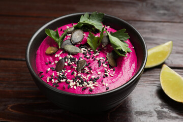 Wall Mural - Tasty beetroot hummus, parsley and seeds in bowl on wooden table, closeup