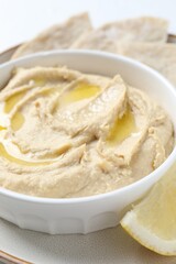 Wall Mural - Delicious hummus with olive oil in bowl and lemon on white table, closeup