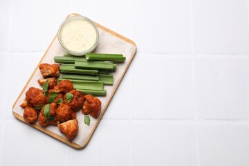 Baked cauliflower buffalo wings with celery and sauce on white tiled table, top view. Space for text