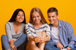 © Prostock-studio - Group of multiracial classmates having break, watching videos on smartphone over yellow background