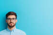 © Weerapat - A thoughtful young man with glasses poses against a vibrant blue background, radiating confidence and style.