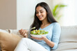 © Niks Ads - attractive indian woman standing and eating salad at the kitchen counter
