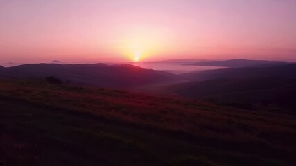 Wall Mural - Clear sky at sunrise over rolling hills warm hues of pink and gold a slow pan across the landscape soft sunlight reflects on dew grass cinematic serene natural atmosphere