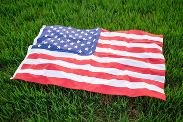 Green fresh grass on the lawn and flag of the USA on it, close up. Concept of proud nationality, patriotism, farming and agriculture in America