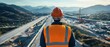 © InnovPixel - A construction worker in a hard hat and reflective vest overlooks a highway project surrounded by mountains, showcasing infrastructure development and engineering