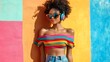 © Galib - A woman with an afro hairstyle wears a striped off-the-shoulder top, jeans, and sunglasses. She's listening to music on headphones while standing in front of a colorful wall.