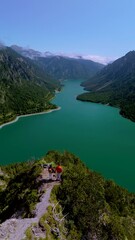 Wall Mural - Plansee Austria, Breathtaking landscape features majestic mountains alongside a vibrant green lake beneath a clear blue sky, a couple of man and woman standing at the viewpoint above the lake Plansee