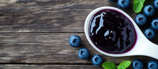 Wall Mural - Top view of blueberry jam in a white spoon over a wooden table with added copyspace for text