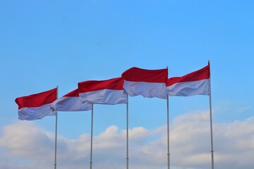 The Indonesian flag waving in the sky with a beautiful background of white fluffy clouds and blue sky.