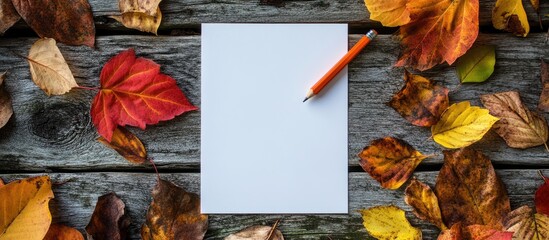 Poster - Blank paper with a pencil surrounded by vibrant autumn leaves on a weathered wooden surface. with copy space image. Place for adding text or design