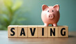 © CheeSiong - Pink piggy bank standing on wooden blocks spelling saving