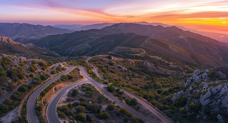 Wall Mural - A winding mountain road leading to the top of the mountains, surrounded by pine forests and snow-capped peaks under the setting sun. 