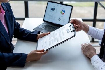 Two people are sitting at a table with a laptop and a clipboard