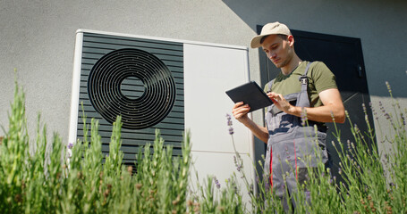 Technician using a tablet to inspect an outdoor heat pump unit on a sunny day.