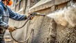 © Four888 - Close-up of a worker's hand operating a pneumatic nozzle, spraying a layer of shotcrete onto a concrete surface, with a dusty, rugged background.