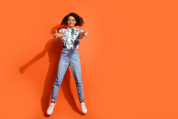 Poster - Full body photo of american woman in jeans and summer stylish shirt jumping trampoline positive rating thumbs up isolated on orange color background