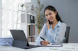 © amnaj - Young asian businesswoman working at her desk in a bright office, talking on the phone and taking notes on documents