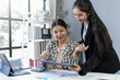 © amnaj - Two businesswomen smiling and working together in the office, analyzing financial documents and digital data on a tablet