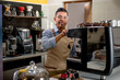 © SALMONNEGRO - Young Latin barista looks at camera and makes coffee on professional coffee machine.