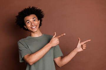 Wall Mural - Photo of youth man t shirt with curly haircut positive directing fingers mockup showing shopping offers for weekend isolated on brown color background