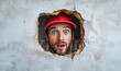 © stockmotion - Junger Mann schaut erschrocken durch ein Loch in der Wand