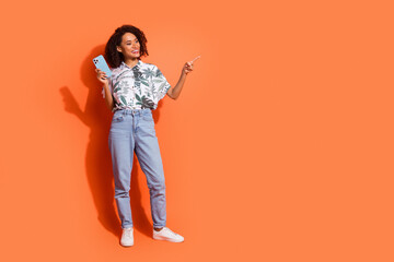 Poster - Photo of brown haired curly girl in summer shirt holding mobile phone pointing finger target advert isolated on orange color background