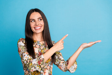 Wall Mural - Photo of adorable lovely girl wear flower print dress pointing holding arm empty space isolated blue color background