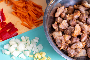 Wall Mural - Fried chopped pork pieces in a bowl next to sliced carrots and onions are prepared for further cooking of pork in a sweet and sour sauce according to a Chinese recipe.