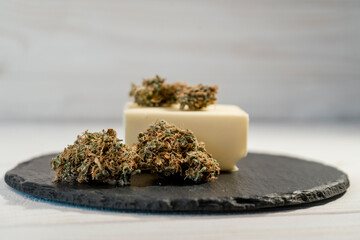 Butter with medical marijuana buds on black cutting board, close up