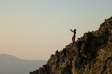 A person is standing on a rocky mountain, taking a picture with their cell phone