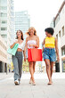 © Jose Calsina - Vertical. Group of young women walking to a store while gossiping. Three girls with shopping bags, laughing and having fun as they take a stroll in the city downtown. Female friends moving to the mall