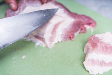 men's hands slice raw pork meat with a large knife on a green board. the process of cooking a meat d