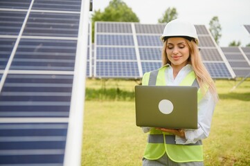 Wall Mural - Portrait of young female engineer standing near solar panels. Beautiful female professional in white helmet