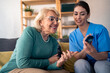 © Dorde - A smiling female nurse in blue scrubs attentively measures the blood glucose level of a happy elderly woman at her cozy apartment, ensuring meticulous in-home patient care.