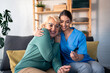 © Dorde - A smiling female nurse in scrubs assists a joyful elderly woman with a glucose test at her home, ensuring compassionate in-home medical support.