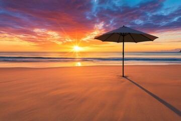 Poster - A beach umbrella casts a long shadow on the sand as the sun sets, painting the sky in vibrant colors while gentle waves lap the shore