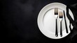 © Paul - Overhead shot of a white plate with neatly aligned fork and knife, black background, strong contrast created by focused studio lighting, extensive copy space.