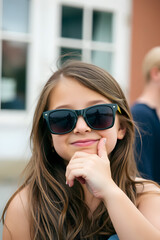 Wall Mural - A young girl wearing stylish sunglasses, smiling confidently. She has a playful expression.