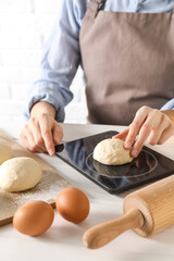 Wall Mural - Woman weighing raw dough ball on kitchen scale at white wooden table, closeup